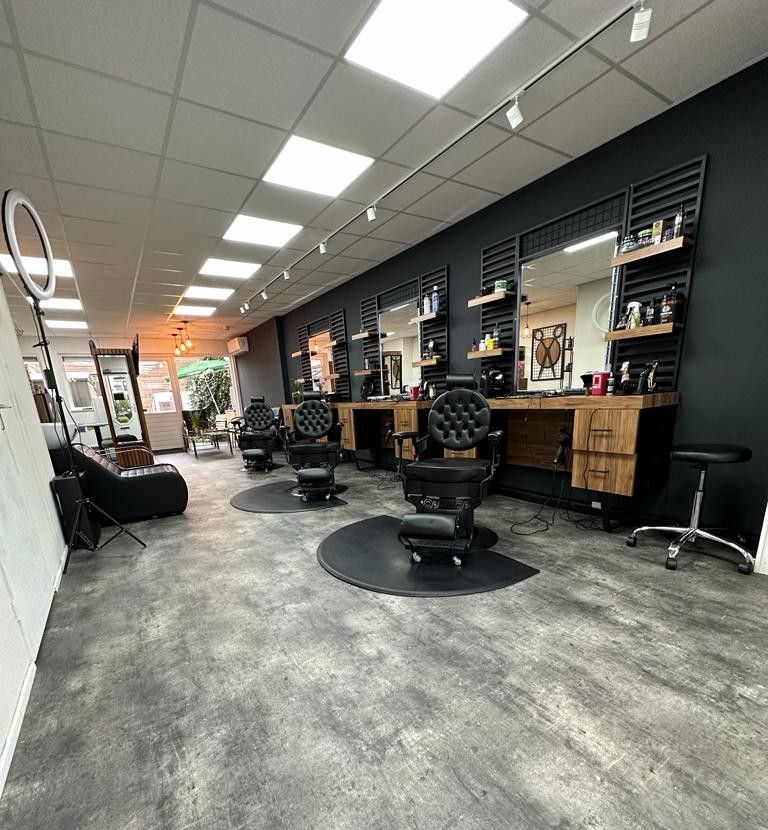 Binnen bij Shaves & Trims: vier zwarte kappersstoelen op ronde matten, houten werkplekken en spiegels langs de zwarte wand